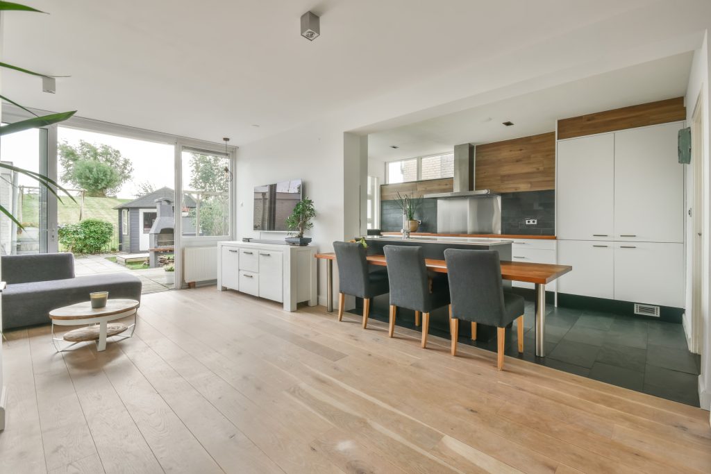 Open living space with a dining area and kitchen, featuring elegant wooden flooring by a renowned flooring installation company, modern furniture, and large windows overlooking a garden.