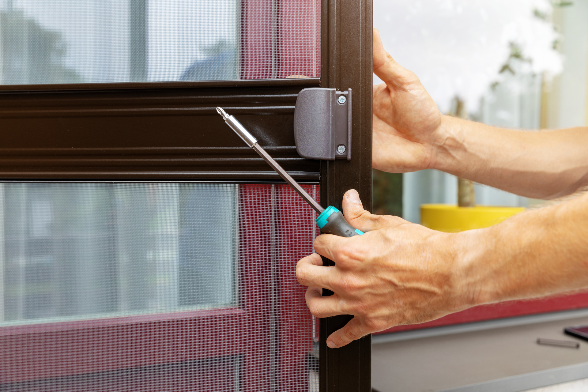 A person from a flooring installation company uses a screwdriver to install or adjust a brown-framed screen door.