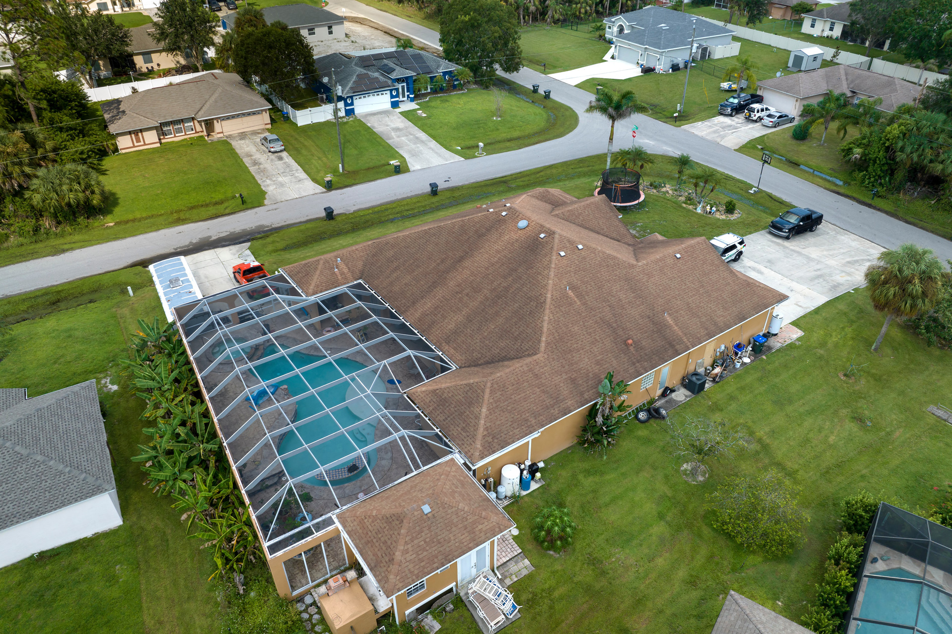 Aerial view of a suburban house with a screened pool area, surrounded by green lawns, trees, and neighboring houses on a curved street. Perfect for families looking in Louisiana or Mississippi, especially if you need advice from a local flooring company.